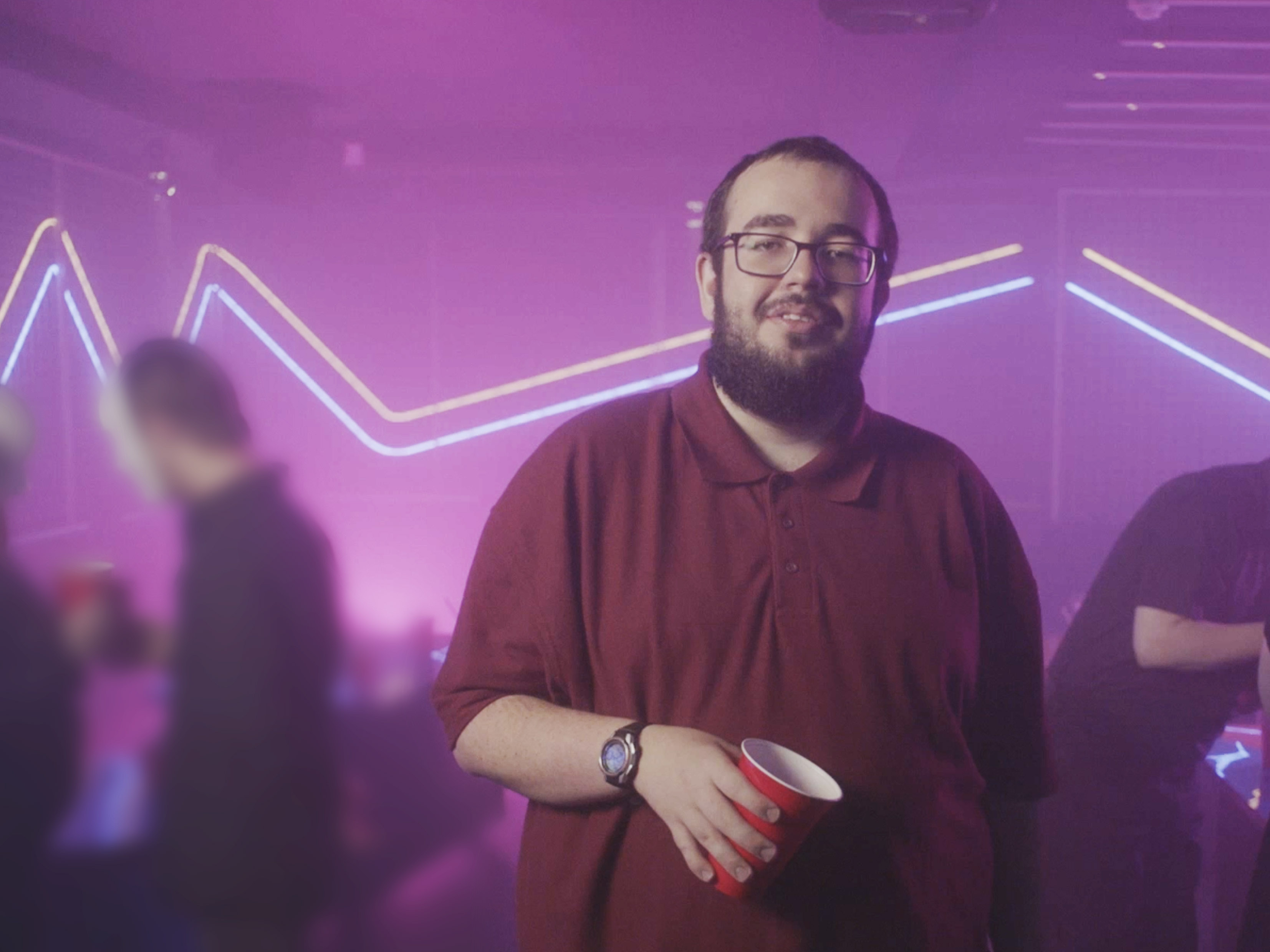 Production still from Typical? showing a man holding a cup in a neon-lit social setting.
